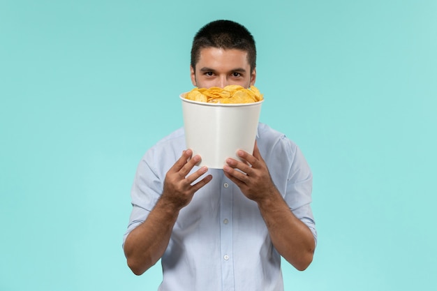 Vista frontal joven sosteniendo la canasta con cips y sonriendo en la pared azul película película remota cine masculino