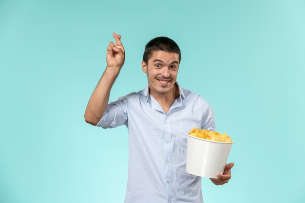 Vista frontal joven sosteniendo la canasta con papas fritas y sonriendo sobre la superficie azul