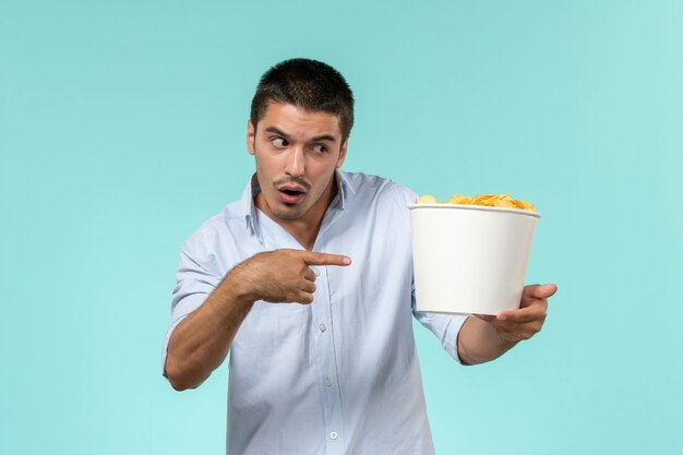 Vista frontal joven sosteniendo la canasta con patatas cips en un escritorio azul cine de película remota macho solitario