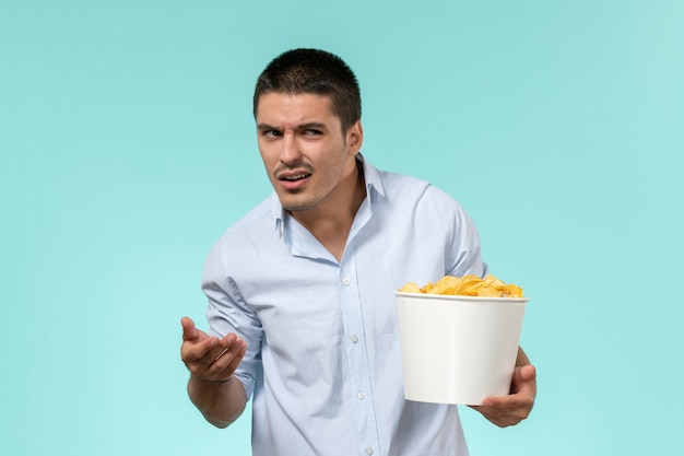 Vista frontal joven sosteniendo la canasta con patatas cips en la pared azul claro cine de película remota macho solitario