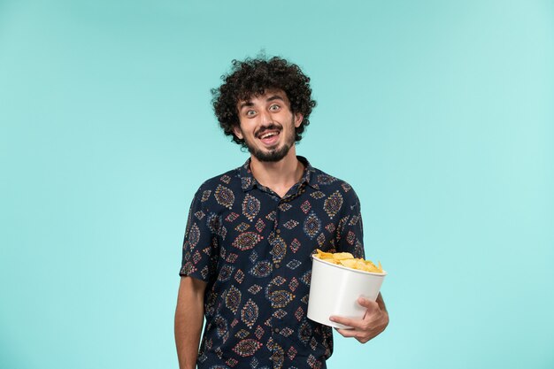 Vista frontal joven sosteniendo la canasta con patatas cips en la pared azul película masculina cine película remota