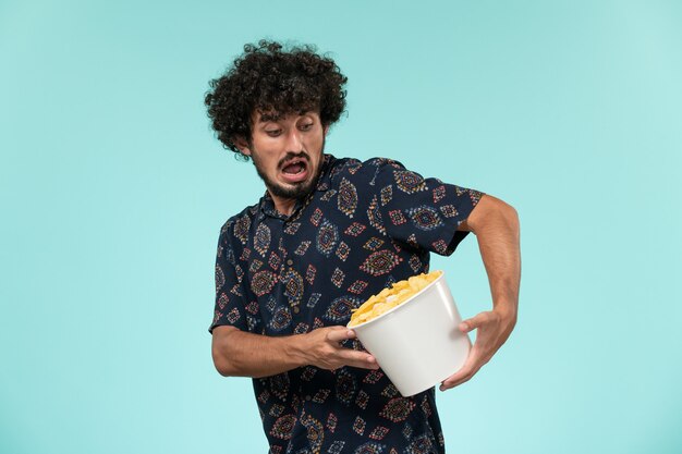 Vista frontal joven sosteniendo la canasta con patatas cips en la pared azul película remota cine cine