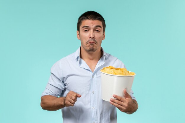 Vista frontal joven sosteniendo una canasta con patatas cips viendo películas y llorando en la película de pared azul claro cine películas remotas