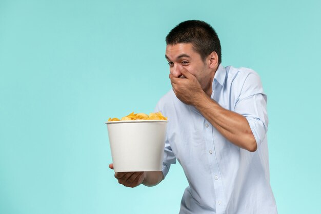 Vista frontal joven sosteniendo la cesta con papas fritas y riendo sobre una superficie azul