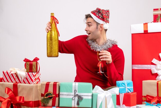 Vista frontal joven sosteniendo champán sentados alrededor de regalos de Navidad