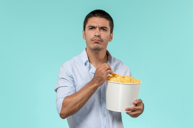 Vista frontal joven sosteniendo cips de papa mientras ve la película en la pared azul cine de cine masculino remoto solitario