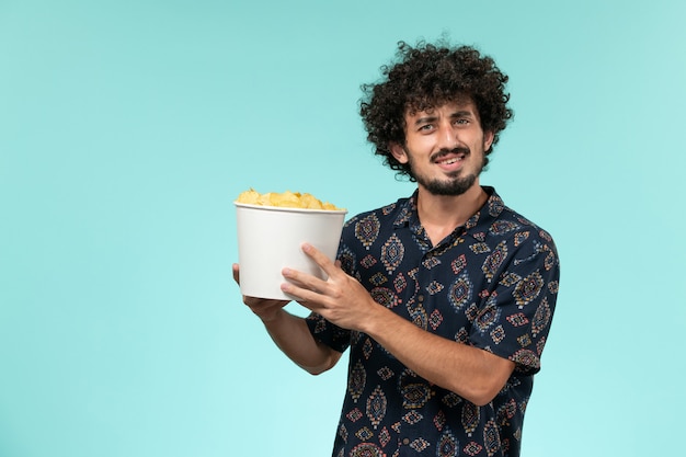 Vista frontal joven sosteniendo cips de patata en un escritorio azul claro cine masculino cine cine