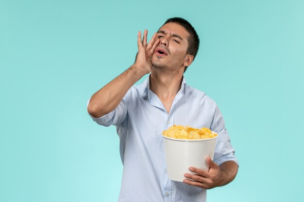 Vista frontal joven sosteniendo cips de patata y llamando a alguien en la pared azul cine películas remotas solitarias