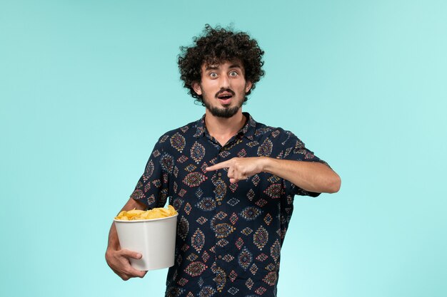 Vista frontal joven sosteniendo cips de patata en una pared azul cine masculino películas cine