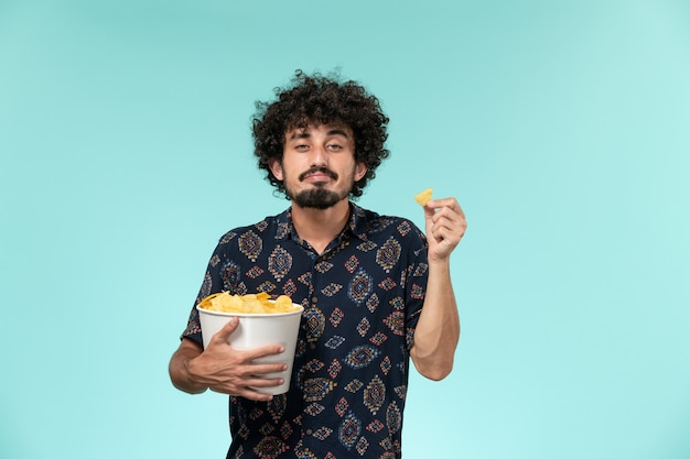 Vista frontal joven sosteniendo cips de patata en la pared azul claro cine películas cine cine masculino