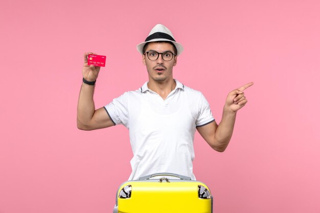 Vista frontal del joven sosteniendo emocionalmente la tarjeta bancaria de vacaciones en la pared rosa