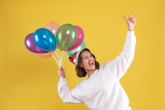 Foto gratuita vista frontal de la joven sosteniendo globos de colores con gran humor en la pared amarilla