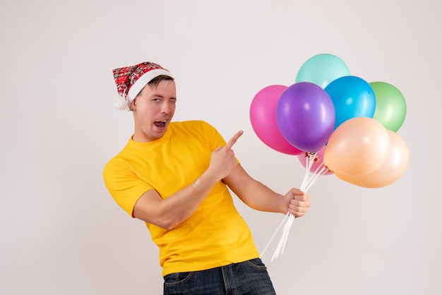 Vista frontal del joven sosteniendo globos de colores en la pared blanca