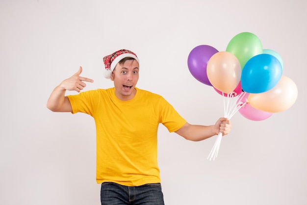 Foto gratuita vista frontal del joven sosteniendo globos de colores en la pared blanca