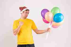 Foto gratuita vista frontal del joven sosteniendo globos de colores en la pared blanca