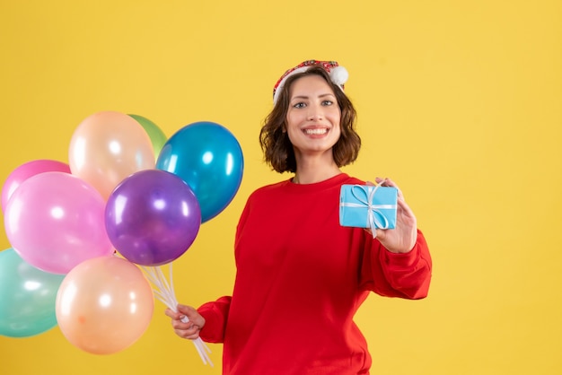 Vista frontal joven sosteniendo globos y poco presente en amarillo navidad vacaciones año nuevo emoción color mujer