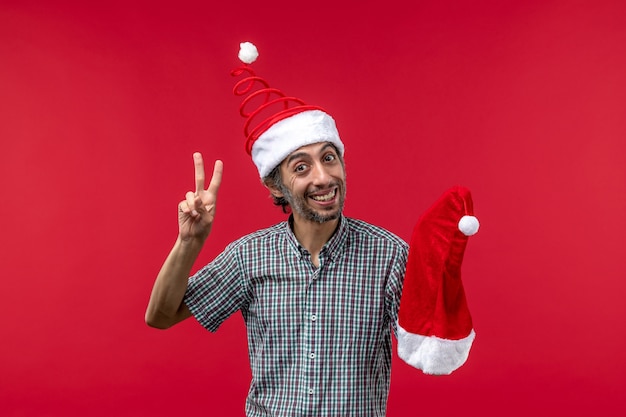 Vista frontal del joven sosteniendo gorro de navidad en la pared roja