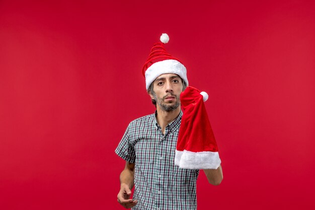 Vista frontal del joven sosteniendo gorro de navidad en la pared roja