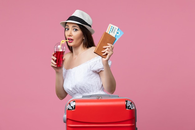 Vista frontal joven sosteniendo jugo y boletos de vacaciones en el escritorio rosa viaje viaje mujer de verano