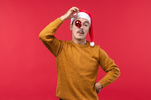 Vista frontal del joven sosteniendo el juguete del árbol de navidad en la pared roja