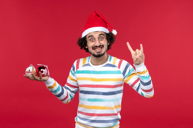 Vista frontal joven sosteniendo juguetes de árbol de navidad en la pared roja año nuevo vacaciones humanas rojas