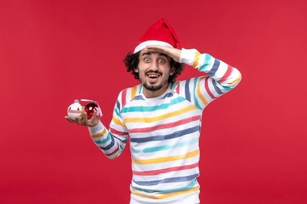 Vista frontal joven sosteniendo juguetes de árbol de navidad en la pared roja vacaciones año nuevo rojo