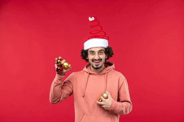 Vista frontal del joven sosteniendo los juguetes del árbol de navidad en la pared roja