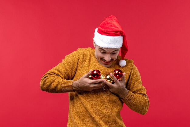 Vista frontal del joven sosteniendo los juguetes del árbol de navidad en la pared roja