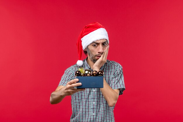 Vista frontal del joven sosteniendo juguetes de árbol de Navidad en rojo