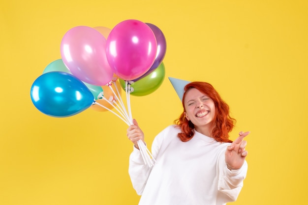 Foto gratuita vista frontal de la joven sosteniendo lindos globos de colores en la pared amarilla