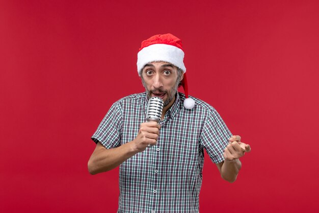 Vista frontal joven sosteniendo el micrófono en la pared roja emociones vacaciones cantante música