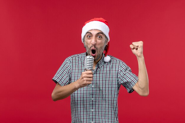 Vista frontal joven sosteniendo el micrófono en la pared roja música cantante de vacaciones de emoción masculina