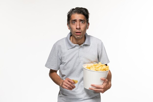 Vista frontal joven sosteniendo papas fritas y viendo la película en la superficie blanca