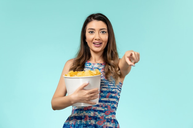 Vista frontal joven sosteniendo el paquete con patatas fritas y viendo la película en la superficie azul