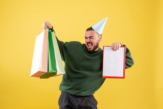 Vista frontal joven sosteniendo paquetes de compras y nota sobre fondo amarillo