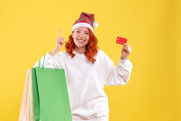 Vista frontal de la joven sosteniendo paquetes de compras y tarjeta bancaria en la pared amarilla