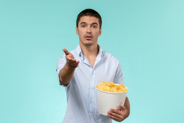 Vista frontal joven sosteniendo patatas cips en una pared azul cine masculino remoto solitario