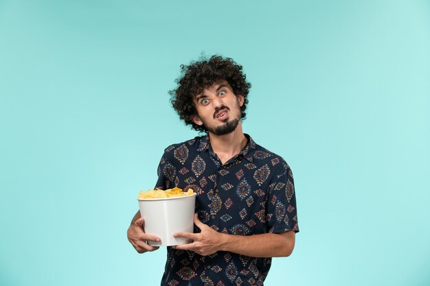 Vista frontal joven sosteniendo patatas cips en la pared azul cine películas cine masculino