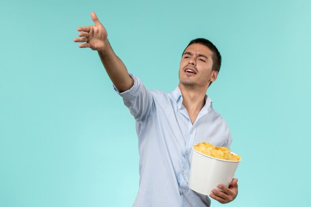 Vista frontal joven sosteniendo patatas cips en la pared azul cine de películas remotas y solitarias