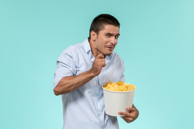 Vista frontal joven sosteniendo patatas cips y viendo películas en la pared azul cine de películas remotas y solitarias