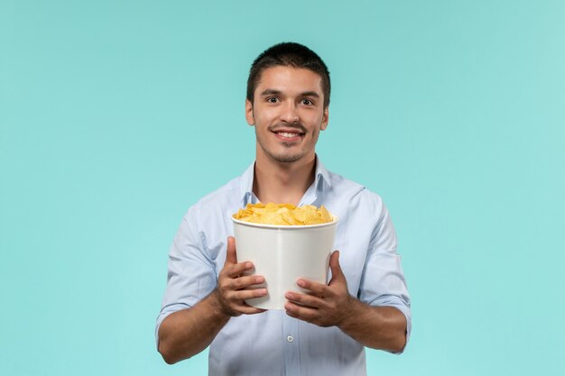 Vista frontal joven sosteniendo patatas cips y viendo películas en la pared azul claro cine de películas remotas y solitarias