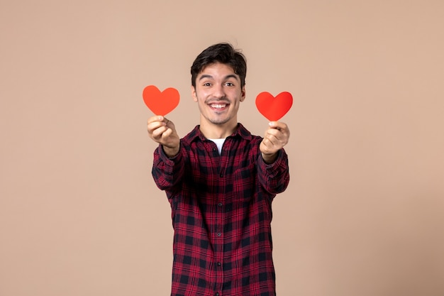 Vista frontal joven sosteniendo pegatinas de corazón rojo en la pared marrón