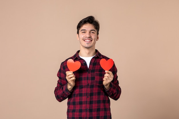 Vista frontal joven sosteniendo pegatinas de corazón rojo en la pared marrón