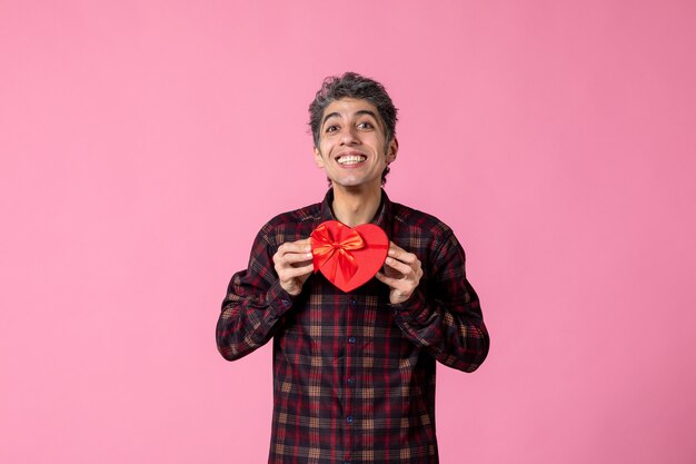 Vista frontal joven sosteniendo presente en forma de corazón rojo en la pared rosa