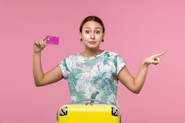 Vista frontal joven sosteniendo púrpura tarjeta bancaria de vacaciones en la pared rosa viaje color vacaciones de verano mujer viaje