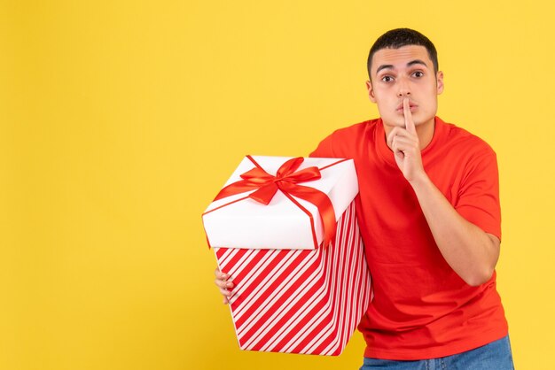 Vista frontal del joven sosteniendo un regalo de Navidad en una pared amarilla