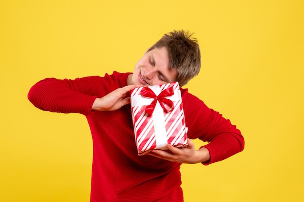 Vista frontal del joven sosteniendo un regalo de Navidad en una pared amarilla