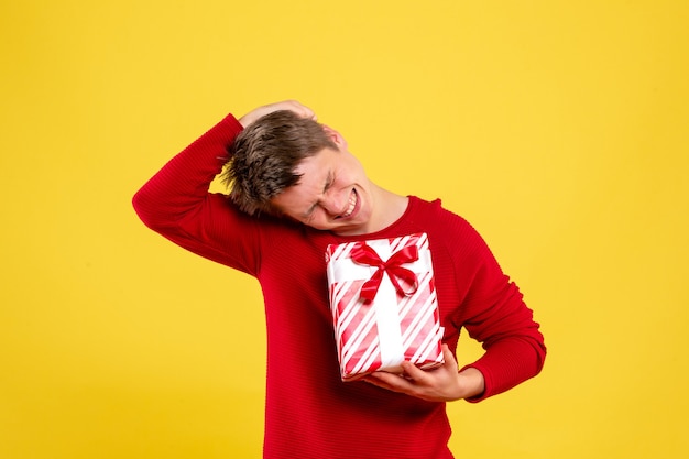 Vista frontal del joven sosteniendo un regalo de Navidad en una pared amarilla