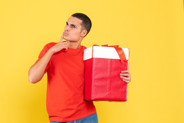 Vista frontal del joven sosteniendo un regalo de Navidad en una pared amarilla