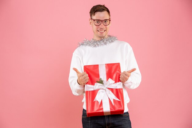 Vista frontal del joven sosteniendo el regalo de Navidad en la pared rosa